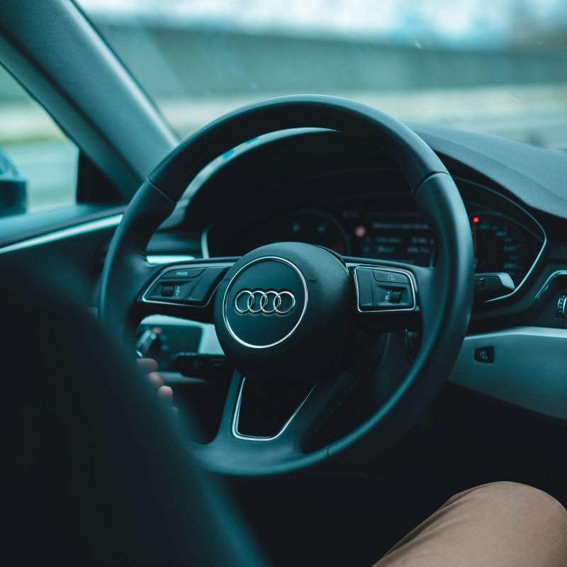 pexels-photo-2277420-2277420 Interior view of a man driving an Audi with focus on steering wheel and dashboard.